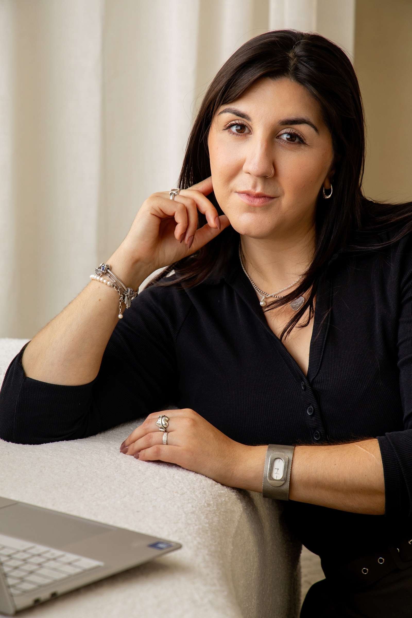 Picture of Faye - a woman with dark hair and eyes leaning against a white couch on her laptop